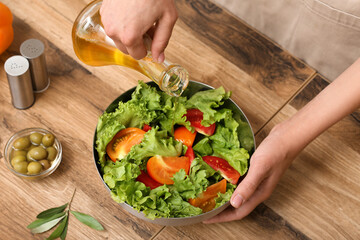 Woman adding olive oil into bowl with tasty salad at table