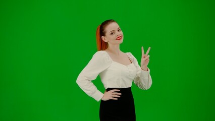 Portrait of attractive office girl on chroma key green screen. Woman in skirt and blouse standing smiling at camera showing victory sign.