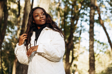 African american woman walking outdoor, portrait of young latin lady in warm sunny autumn park season, fall, yellow orange red leaves, dressed white jacket, having fun smiling laughing
