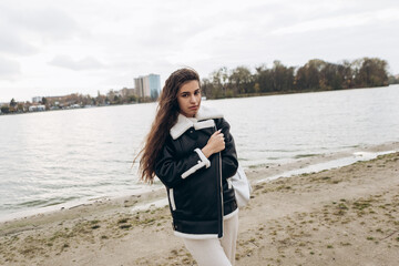 Attractive pretty woman walking outdoor sandy beach shore, portrait of young lady dressed leather wool fur jacket smiling having fun, cold weather windy autumn spring. Loneliness, sadness, sensual
