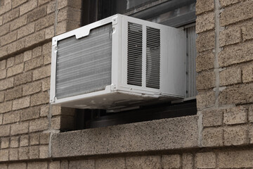 exterior view of air conditioning window unit extruding from the window sill of a brown brick building