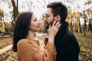 Heterosexual caucasian young loving couple walking outside in the city park in sunny weather, hugging smiling kissing laughing spending time together. Autumn, fall season, orange yellow red maple leav