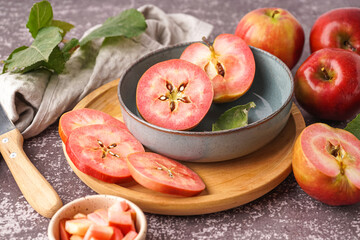 Bowl and wooden board with sweet pink apples on dark background