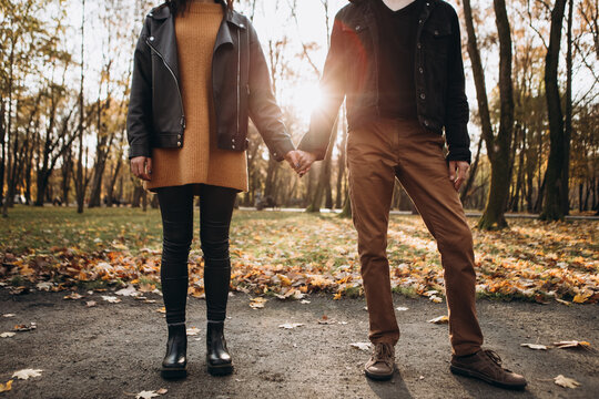 Cropped image hands young loving couple walking outside in the city park in sunny weather, hugging smiling kissing laughing spending time together. Autumn, fall season, orange yellow red maple leaves
