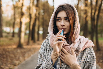 Young woman outside autumn park fall and smoking tobacco device electronic cigarette heater. Smoke...