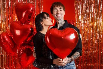 Young couple with balloon against tinsel on red background. Valentine's Day celebration