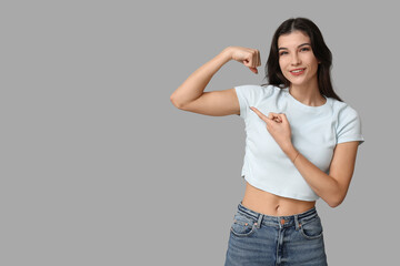 Young woman flexing muscles on grey background. Feminism concept