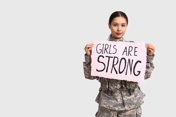 Young female soldier with sign GIRLS ARE STRONG on white background. Feminism concept