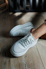 Close-up of female legs in white perforated leather sneakers. Women's summer sneakers. Collection...