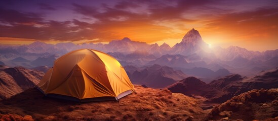 The dome tent is illuminated by the warm light of the rising sun as the golden cloudscape reveals dramatic mountain peaks from a panoramic landscape with blue, purple and orange skies - obrazy, fototapety, plakaty