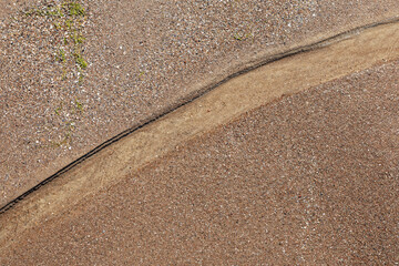 Sea sand texture with diagonal line of flowing water, shot from above