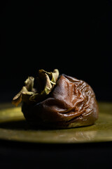 A dark, wrinkled and rotting persimmon fruit against a black background.