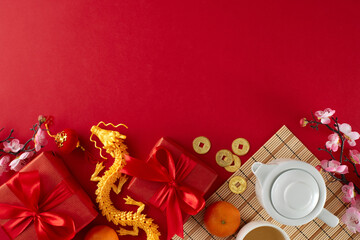 Marking chinese New Year with a tea ceremony celebration. Top view flat lay of teapot, cup of tea, tangerines, gold dragon, gift boxes, traditional chinese decor on red background with advert space