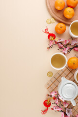 Obraz na płótnie Canvas Exploring the сhinese New Year tea ceremony. Top view vertical shot of teapot, cups of tea, mandarins, sakura, lanterns, gold coins on beige background with advert zone