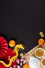 Adopting the essence of the chinese New Year tea ceremony. Top view vertical shot of teapot, cups of tea, tangerines, folding fans, gold dragon, chinese decor on black background with ad space