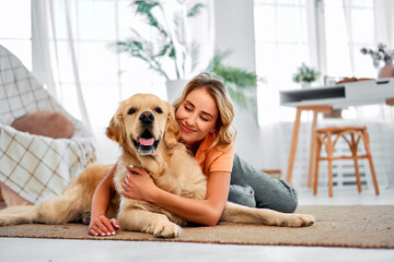 Love to pet. Adorable woman with closed eyes embracing adult golden retriever while lying together on floor.