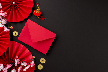Gift suggestions for Chinese New Year festivities. Top view photo of red envelope, folding fans, sakura, traditional coins, lanterns on black background with advert spot