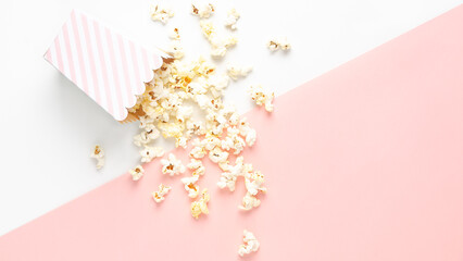 A striped bucket of popcorn on white and pink background, top view and copy space. 