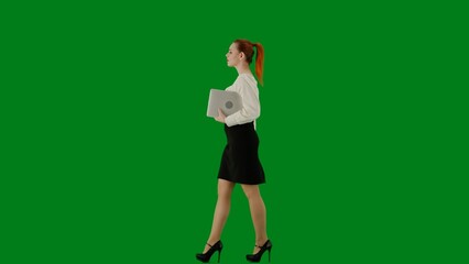 Fototapeta na wymiar Portrait of attractive office girl on chroma key green screen. Woman in skirt and blouse walking holding laptop. Side view.