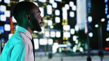 Businessman admiring skyscrapers at night, walking around city center with streetlights. African...