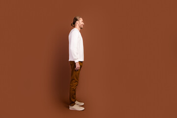 Fototapeta na wymiar Full length photo of handsome positive man wear white sweater looking empty space isolated brown color background