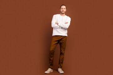Fototapeta na wymiar Full length photo of cheerful confident man wear white sweater smiling arms crossed isolated brown color background