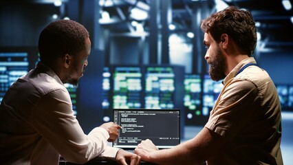 IT developers team writing server script code in data center on laptop terminal. Teamworking...