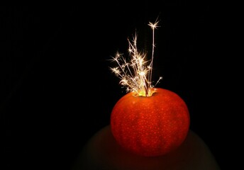 A burning sparkler stuck in a tangerine, a fancy trick for festive occasions