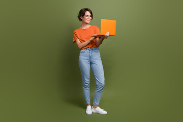 Full size photo of positive smart woman wear t-shirt jeans in glasses look at laptop write email isolated on khaki color background