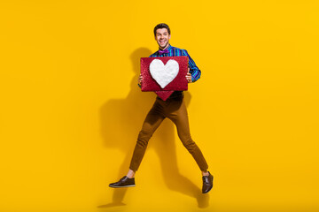 Fototapeta na wymiar Full size photo of cheerful guy dressed striped shirt jumping with big social media like box in arms isolated on yellow color background