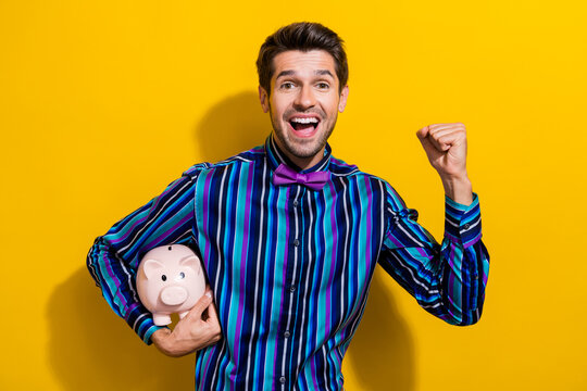Photo of overjoyed guy with stubble dressed striped shirt hold monye box raising fist up win bet isolated on yellow color background
