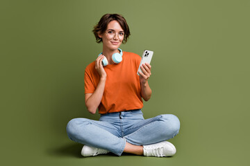 Full size photo of lovely woman wear t-shirt in glasses sit on floor listen playlist in smartphone...