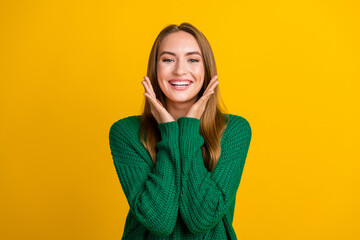 Photo portrait of attractive young astonished cute lady wearing green jumper touch cheeks seems happy isolated on yellow color background