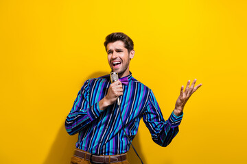 Photo of handsome man dressed striped shirt bow tie sing pop song in microphone on scene at party isolated on yellow color background - Powered by Adobe