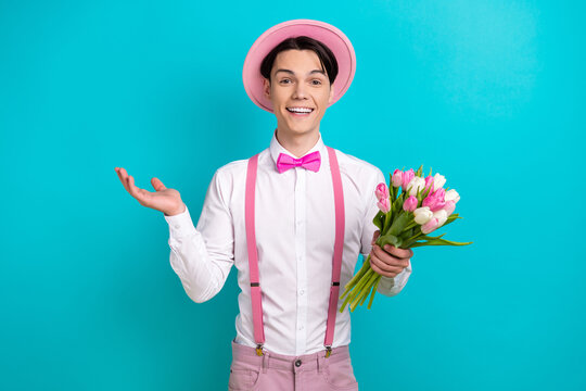 Portrait of handsome optimistic man dressed pink cap bow tie hold bouquet wish you happy birthday isolated on blue color background