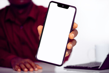 Black man holding and showing smartphone with blank screen close to camera isolated over white...