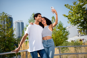 Photo of cheerful cute married couple dressed casual outfits recording video vlog modern gadget outdoors urban city park