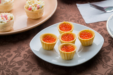 Red caviar in tartlets on a plate on a brown tablecloth