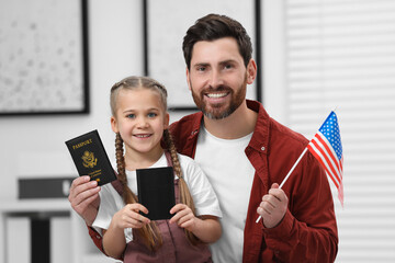 Immigration. Happy man with his daughter holding passports and American flag indoors
