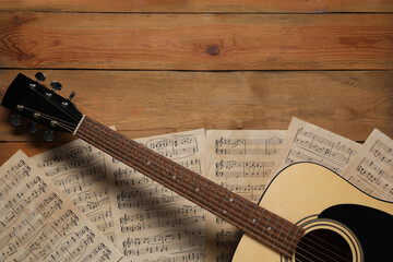 Paper sheets with music notes and acoustic guitar on wooden table, top view