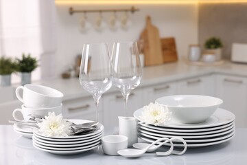 Set of clean dishware, glasses, cutlery and flowers on table in kitchen