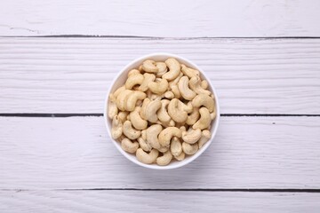 Tasty cashew nuts in bowl on white wooden table, top view
