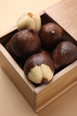 Wooden crate with fresh salak fruits on beige background, closeup