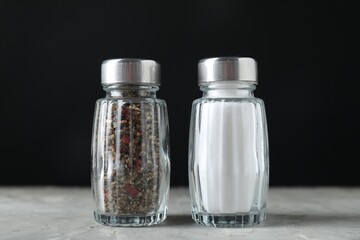 Salt and pepper shakers on light table against black background, closeup