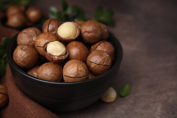Tasty Macadamia nuts in bowl on brown table, closeup. Space for text