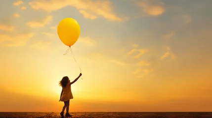 Fotobehang silhouette of girl holding a yellow balloon with a sunset in the background © Favio