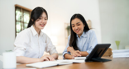 Two cheerful  workers women cooperating on project, sitting at work desk with laptop, looking at screen, smiling,