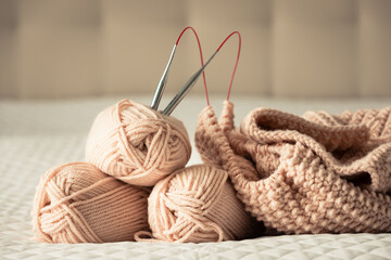 Obraz premium Knitting yarn, needles, chunky sweater. Cozy homely atmosphere. Yarn in warm colors of peach, beige. Knitting as a hobby. Accessories for knitting.