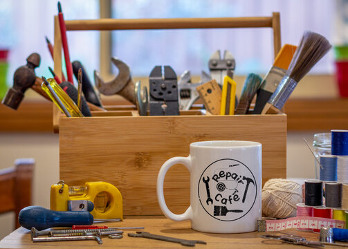 Repair Cafe logo mug with repair tools on table in cafe used as a repair centre consumer activism to repair household items to reduce waste and support a sustainable lifestyle