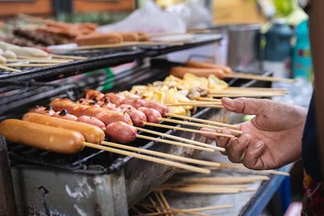 Foto op Plexiglas Thai Street Food, Delicious Grilled Sausage and Meatballs and squid Wood Skewers Menu, Grilled on Charcoal grill. Selling along the Road side in Bangkok city. © Kanthita